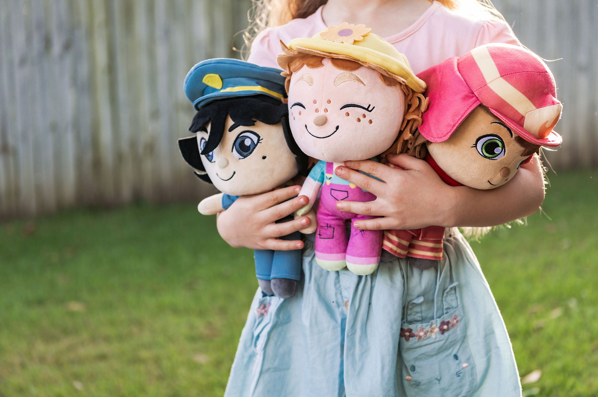 Child holding three plush toys outdoors