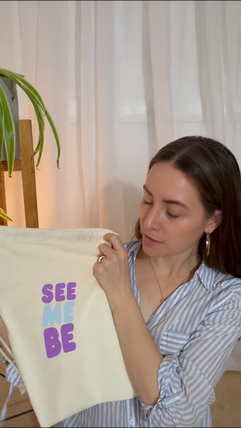 See Me Be Toys natural cotton drawstring bag held up to show its printed logo.